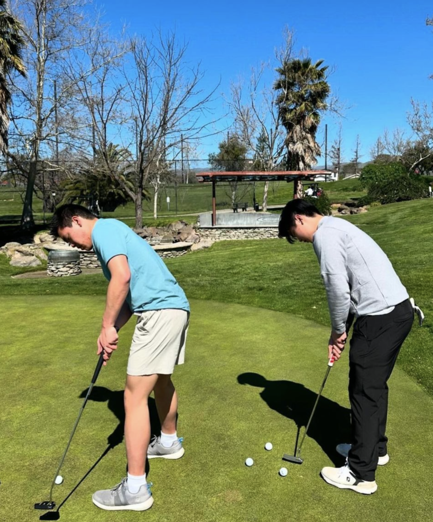 Senior Ryan Lin and Sophomore Miles Sy line up on the putting green and prepare to hit a golf ball during practice
